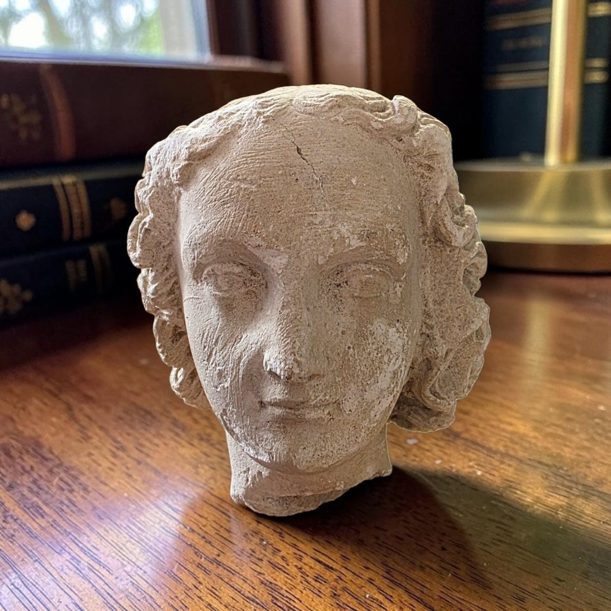 Late Gothic carved limestone head of a youth from Champagne, France, c.1500–1540, shown on a mahogany desk with leather-bound books
