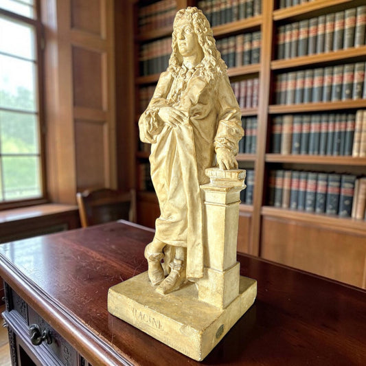 19th-century patinated plaster figure of the French dramatist Jean Racine, standing and leaning on a pedestal, displayed on a desk in a book-lined library