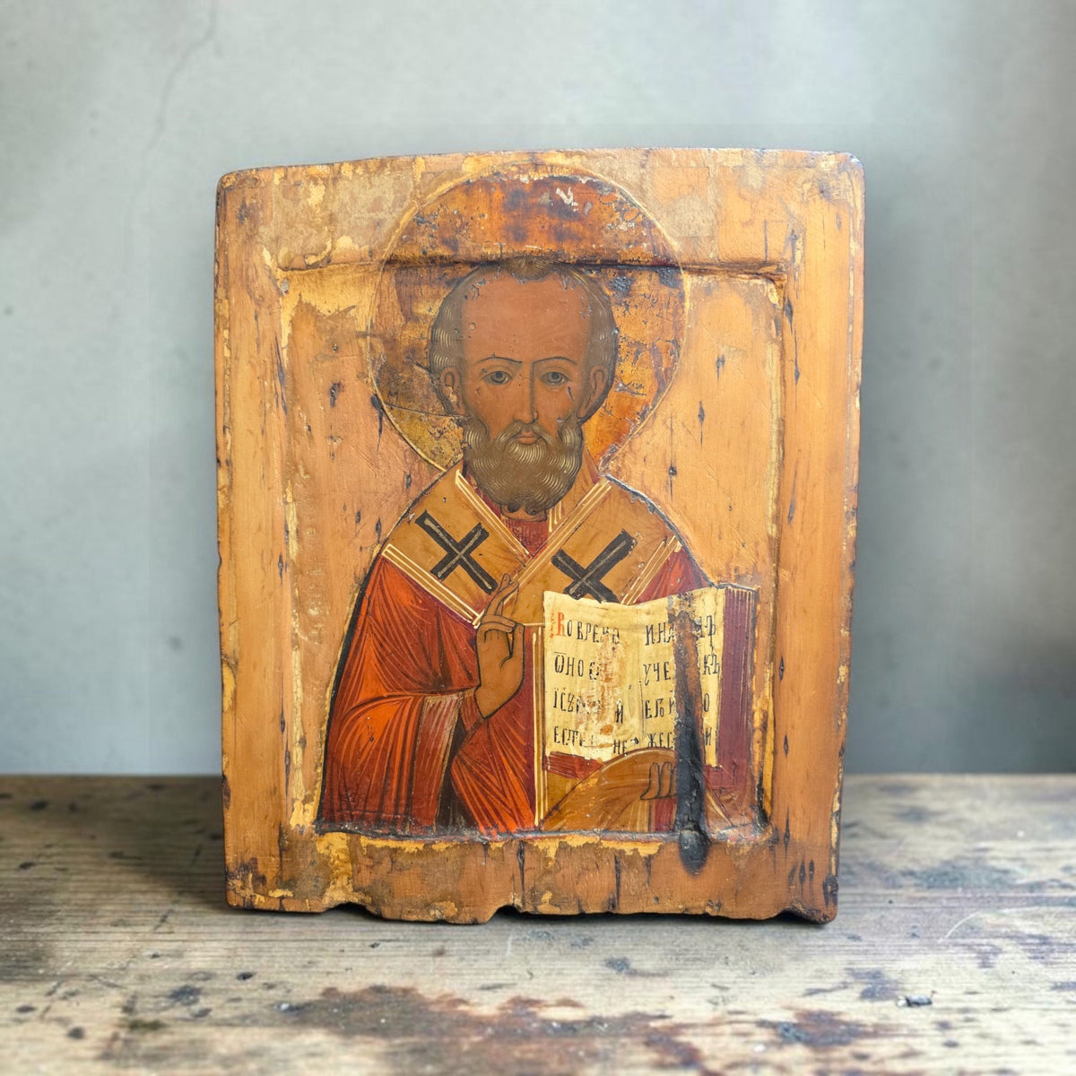 Antique Russian icon of Saint Nicholas standing on a weathered table against a grey plaster wall