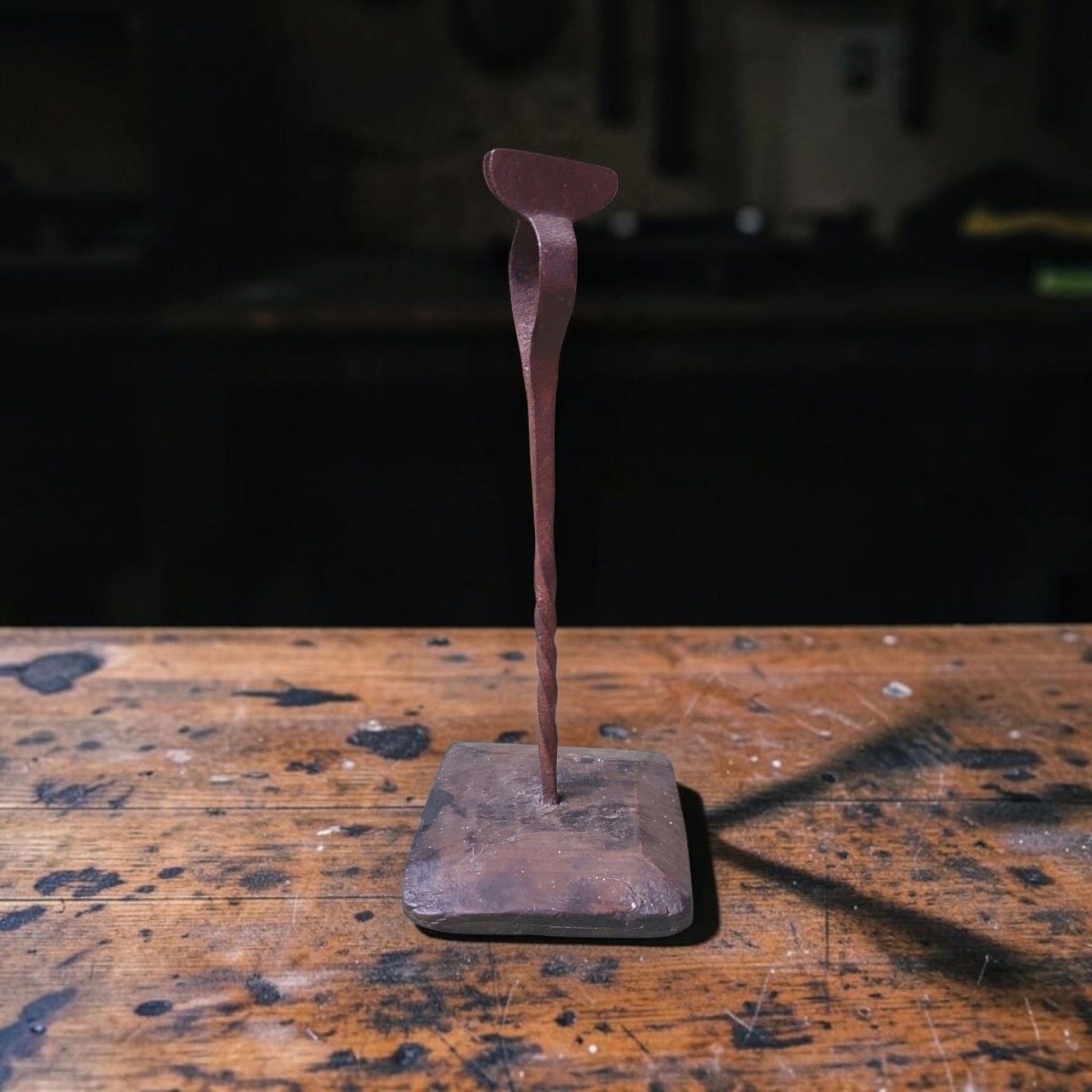 Antique wrought iron rushlight holder or peerman with spiral-twist stem on a rectangular wood base, on a workbench