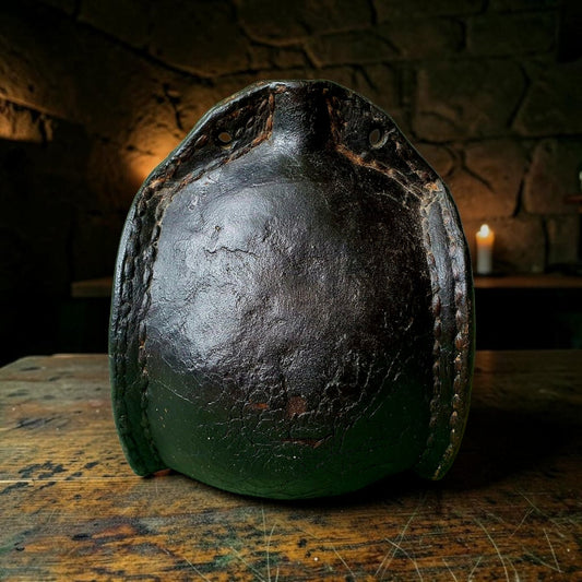 17th century leather costrel with stitched seams, on a wooden table beside a lit candle