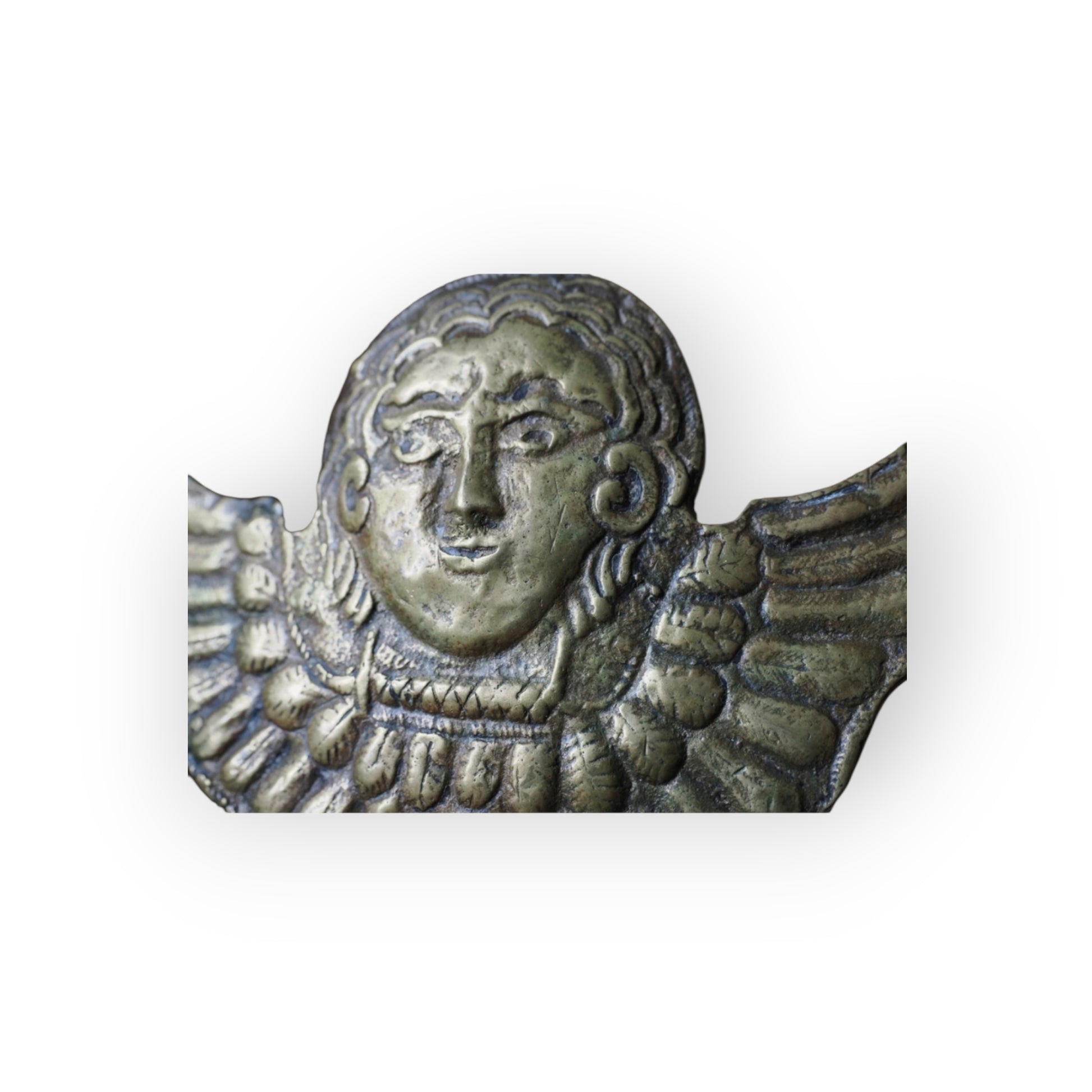 Detail of naive cast cherub face with curled hair and scrolled ears on Renaissance brass appliqué.