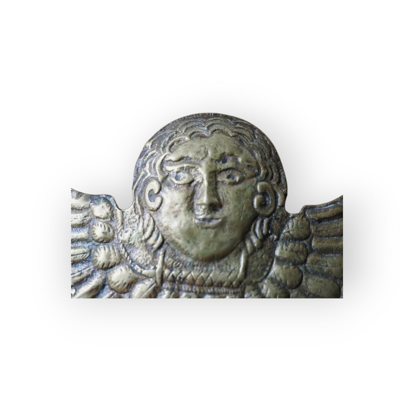 Detail of naive cast cherub face with curled hair and scrolled ears on Renaissance brass appliqué.